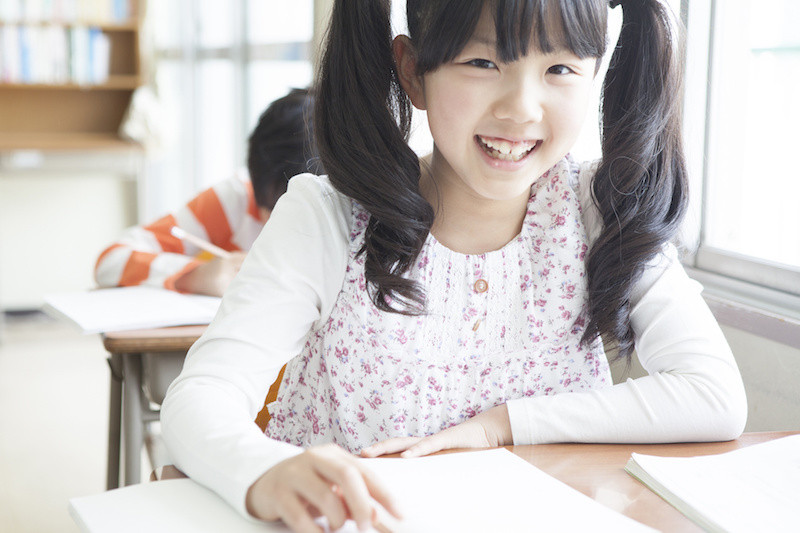 教室で机に向かい笑いかけている女児